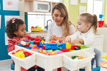 Teacher with girls playing with construction blocks sitting on table at kindergarten