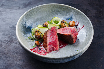 Rohes italienisches Rinderfilet Steak vom Chianina Rind mit Pilzen, Zucchini and Amarena Sauce serviert als close-up in einer Nordic Design Schale
