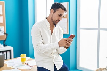 Young hispanic man business worker using smartphone at office