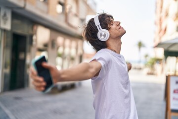 Young blond man smiling confident listening to music at street