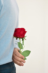 Photo of man holding a red rose behind his back.