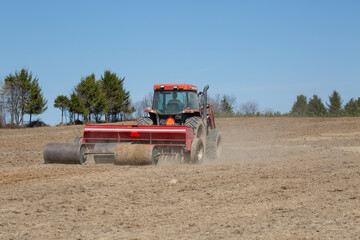 Farmer is sowing seeds with agricultural seeder on a beautiful spring day.  Agricultural machinery equipment on farm. 