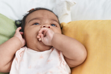 African american baby sitting on bed sucking hand at bedroom