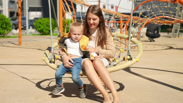 Little baby boy getting upset and refusing swinging in swing with mother. Children playing outdoor, kids outside, summer holiday and vacation