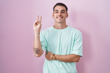 Handsome hispanic man standing over pink background smiling with happy face winking at the camera...