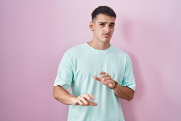 Handsome hispanic man standing over pink background disgusted expression, displeased and fearful...
