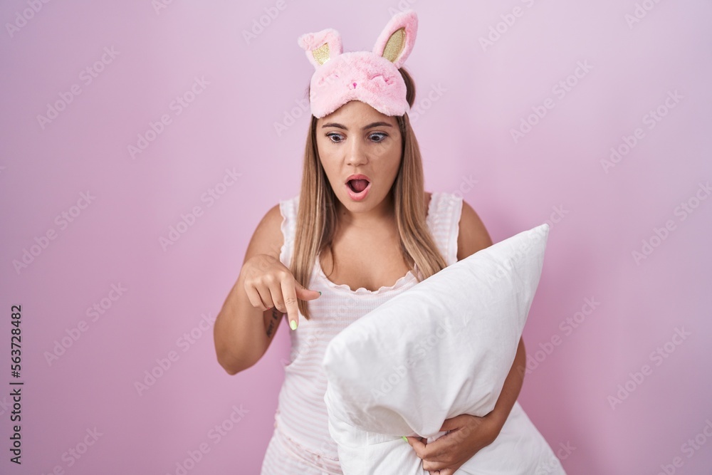 Sticker Young blonde woman wearing pyjama hugging pillow pointing down with fingers showing advertisement, surprised face and open mouth