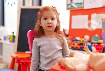 Adorable redhead girl sitting on table with serious expression at kindergarten