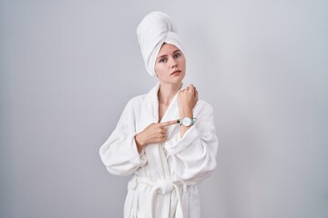 Blonde caucasian woman wearing bathrobe in hurry pointing to watch time, impatience, looking at the camera with relaxed expression - obrazy, fototapety, plakaty