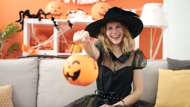 Young blonde woman wearing halloween costume holding pumpkin basket at home