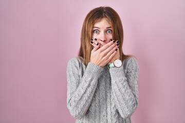 Beautiful woman standing over pink background shocked covering mouth with hands for mistake. secret...