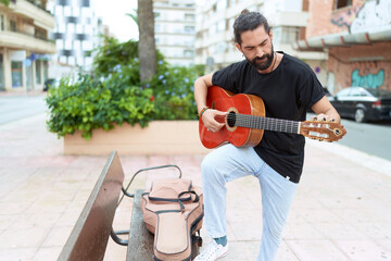 Young hispanic man musician playing classical guitar at park