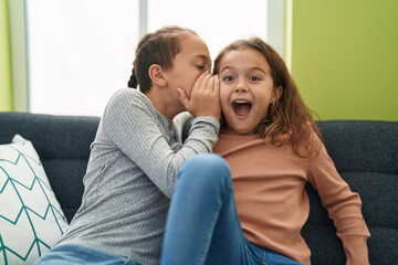 Two kids telling secret sitting on sofa at home