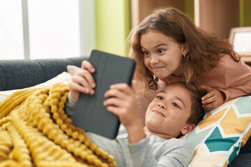 Two kids watching video on touchpad lying on sofa at home