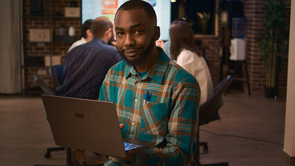 African american office employee working on laptop portrait, front view. Smiling man holding computer, looking at camera medium shot, company financial presentation, business meeting