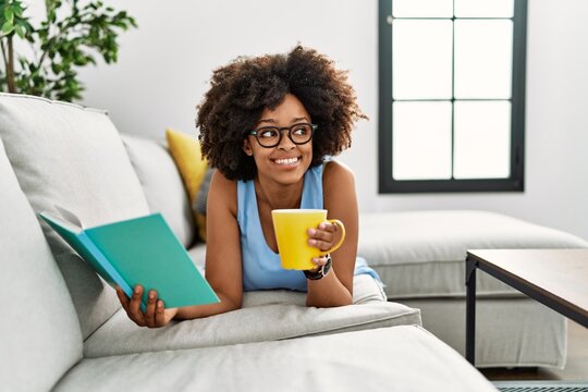 Young african american woman drinking coffee reading book at home