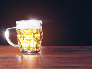 Full jar of lager beer with froth on a wooden table glowing in a dark. Alcohol consumption and sale. Copy space. Light flare.