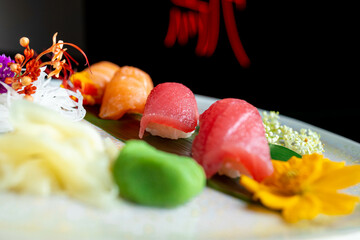 four nigiri sushi with salmon and tuna served on fresh green banana leaf on black background with japanese sign © leo
