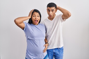 Young hispanic couple expecting a baby standing over background crazy and scared with hands on head, afraid and surprised of shock with open mouth