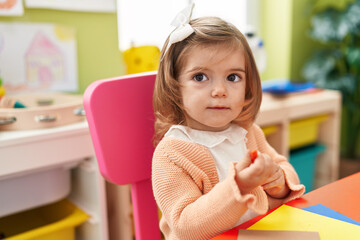 Adorable blonde toddler preschool student sitting on table drawing on paper at kindergarten