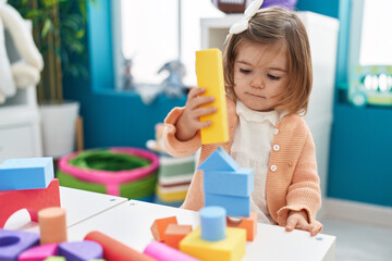 Adorable blonde toddler playing with construction blocks standing at kindergarten
