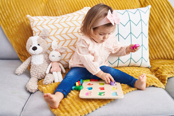 Adorable blonde toddler playing with maths puzzle game sitting on sofa at home