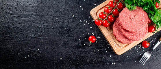 A raw burger on a tomato cutting board. 