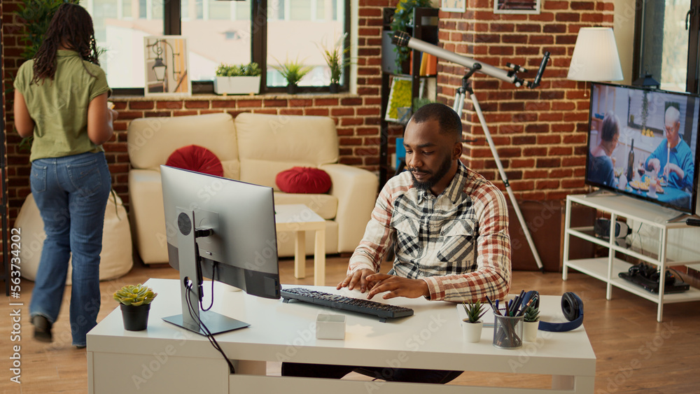 Poster african american man working on computer at desk, doing remote task at home with girlfriend. young a