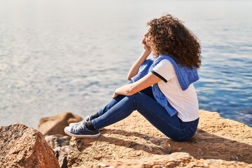 Young hispanic woman relaxed sitting on rock at seaside