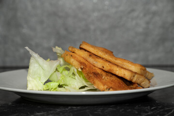 Close-up of freshly fried panelle, a Sicilian specialty made from chickpea flour. The panels are served on a green salad. The background is grey.