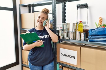 Young blonde girl wearing volunteer uniform talking on the smartphone at charity center