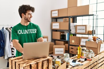 Young hispanic man wearing volunteer uniform using laptop at charity center