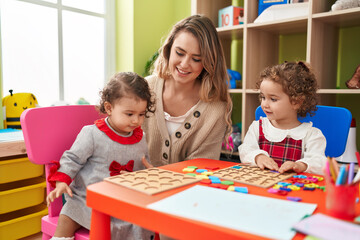 Fototapeta premium Teacher with girls playing with maths puzzle game sitting on table at kindergarten
