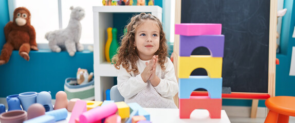 Adorable blonde toddler playing with construction blocks clapping hands at kindergarten