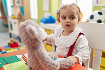 Adorable blonde toddler playing with teddy bear sitting on table at kindergarten