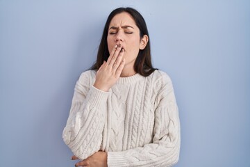 Young brunette woman standing over blue background bored yawning tired covering mouth with hand. restless and sleepiness.