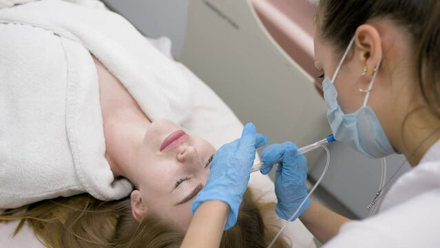 cosmetologist performs a gas-liquid peeling procedure - rejuvenation and regeneration of the skin using a jet consisting of oxygen and liquid.