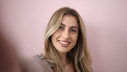 Fototapeta premium Young blonde woman smiling confident making selfie by camera over isolated pink background