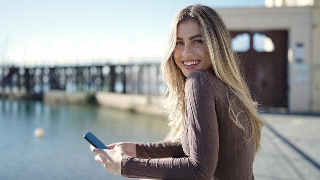 Young blonde woman smiling confident using smartphone at seaside