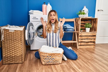 Young blonde woman doing laundry at home celebrating victory with happy smile and winner expression with raised hands