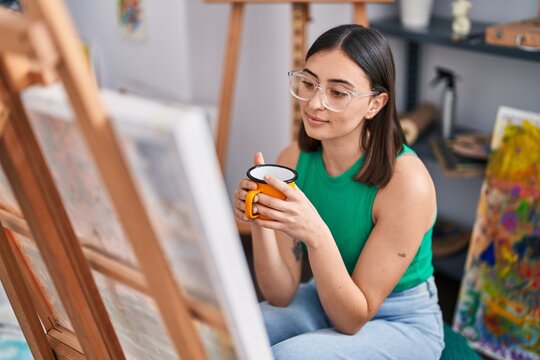 Young hispanic woman artist drinking coffee at art studio
