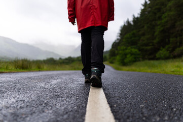 Detailed photo of a person´s legs while crossing a road with fir trees in the background during a foggy day in the highlands, Scotland