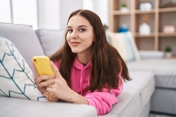 Young woman using smartphone lying on sofa at home