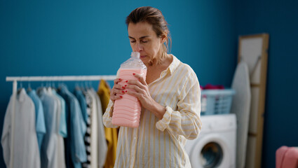 Middle age hispanic woman smelling detergent at laundry room