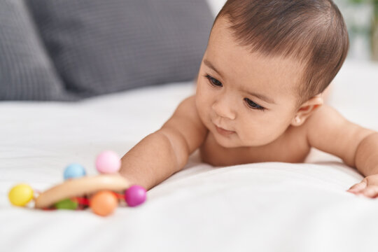 Adorable hispanic baby lying on bed holding rattle at bedroom