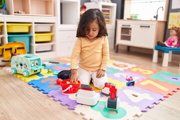 Adorable hispanic toddler playing with supermarket toy sitting on floor at kindergarten
