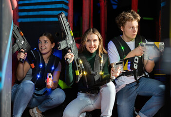 Modern satisfied young people with laser pistols playing laser tag on dark labyrinth