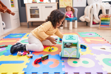 Adorable hispanic toddler playing with car toy sitting on floor at kindergarten