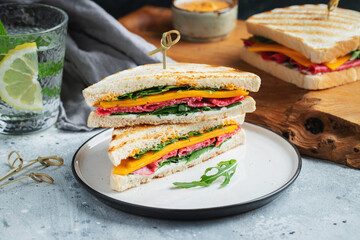 Two homemade sandwiches with sausage, cheese and arugula on a light concrete background