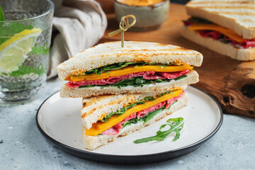 Two homemade sandwiches with sausage, cheese and arugula on a light concrete background